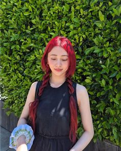 a woman with red hair holding a white frisbee in front of some bushes