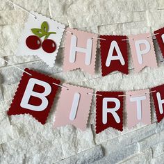 a happy birthday banner with cherries hanging from it's sides on a brick wall