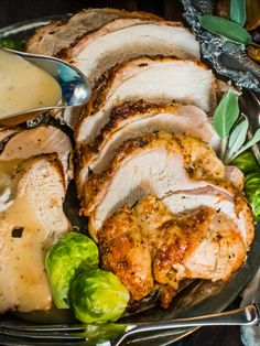 a plate full of meat and vegetables with gravy on the side next to silverware