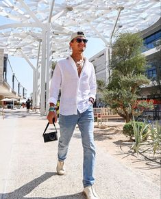 a man in white shirt and jeans holding a black bag walking down the street under an awning