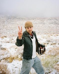 a man standing in the middle of a field with his hand up and two fingers out