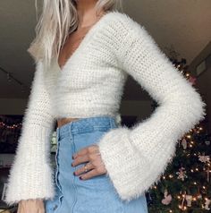 a woman with blonde hair is standing in front of a christmas tree wearing a white sweater and jeans