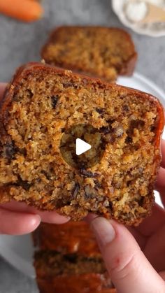 a person holding a piece of bread with raisins on it and carrots in the background