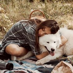 a woman laying on top of a blanket next to a white dog