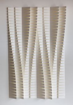 an abstract piece of art made out of strips of white paper on a wall in a room