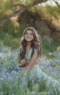 a beautiful young woman sitting in a field of blue flowers