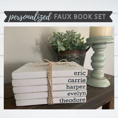 a stack of white books sitting on top of a wooden table next to a candle