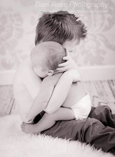 a black and white photo of a boy hugging his baby