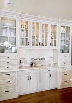 a kitchen with lots of white cabinets and glass doors on the cupboards in it