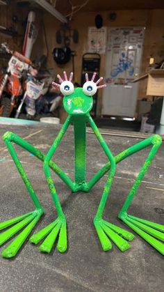 a green frog made out of plastic sitting on top of a table in a garage