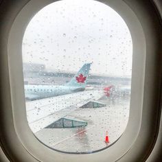 looking out an airplane window at airplanes on the tarmac and in the distance, rain drops