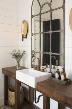 a bathroom sink sitting under a large mirror next to a wooden table with bottles on it