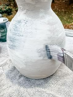 a white vase sitting on top of a table next to a can of paint and a brush