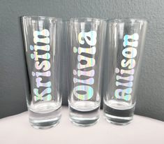 three shot glasses with the words happy holidays on them are sitting side by side in front of a gray wall