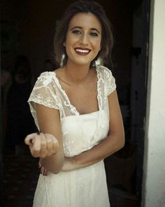 a smiling woman in a white dress pointing at the camera with her right hand out