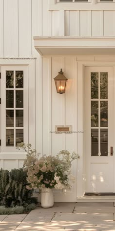 the front door of a white house with potted plants and lights on it's side