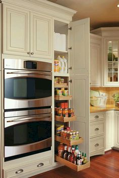 an open cabinet in the middle of a kitchen with two ovens and spice racks