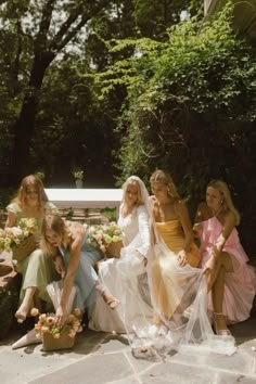 a group of women sitting next to each other on top of a stone floor in front of trees