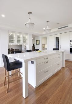 a large white kitchen with an island in the middle and two black chairs at the end