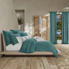 there is a bed with teal colored sheets and pillows on the wooden flooring