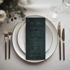 a place setting with silverware and green menu cards on the plate, along with gold cutlery