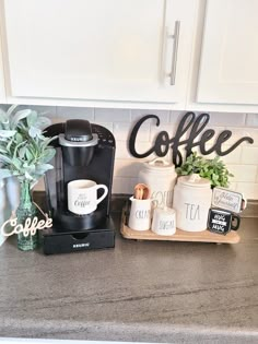 the coffee maker is sitting on the counter next to some mugs and potted plants