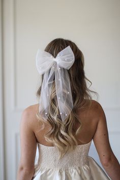 the back of a bride's dress with a white bow on her head and hair