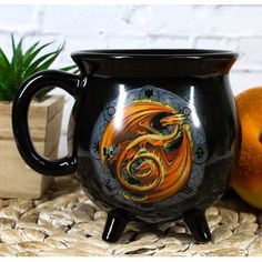 a dragon mug sitting on top of a table next to two peaches and an orange