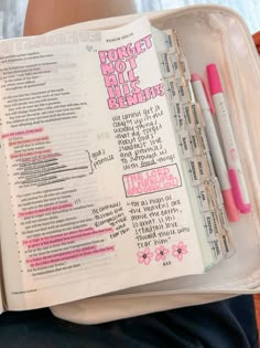 an open bible with pink writing on it and some pens in the bottom half of the book