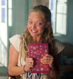 a woman holding up a pink book with flowers on it and smiling at the camera