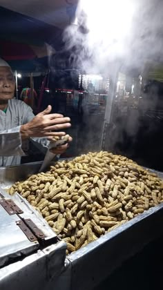 a man is cooking peanuts in a large frying pan with steam coming out of it