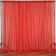 a red curtain hanging on the side of a white wall next to a wooden floor