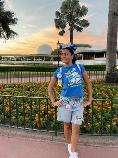 a woman standing in front of a flower garden with flowers around her and palm trees behind her