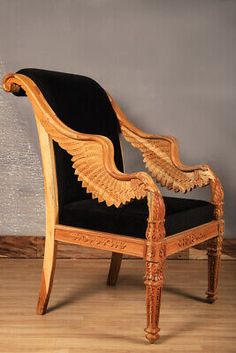 an ornate wooden chair with black velvet upholstered seat and arm rests against a wall