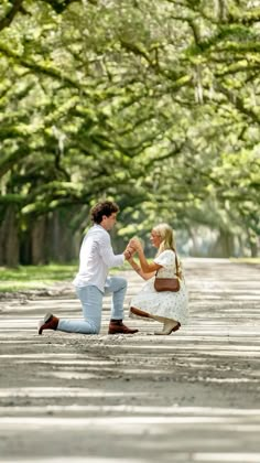 a man kneeling down next to a woman in the middle of a road with trees