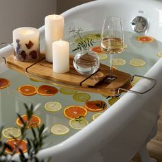 an oval bathtub with candles and orange slices on the bottom, next to a glass of wine