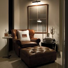 a living room with a chair, ottoman and lamp on the side table in front of a window