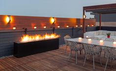 a fire pit on top of a wooden deck next to chairs and tables with lit candles