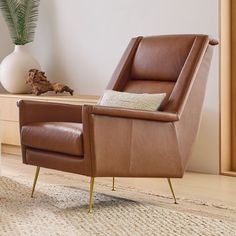 a brown leather chair sitting on top of a wooden floor next to a white vase