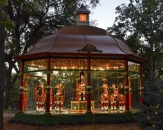 a merry go round with lights and decorations on the top, in front of some trees