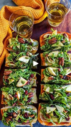 several slices of bread topped with green vegetables and nuts next to two glasses of beer