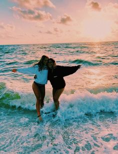 two women are standing in the water at the beach with their arms around each other