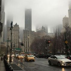 cars are driving down the street in front of tall buildings on a foggy day