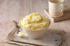 mashed potatoes in a white bowl on a wooden table next to a cup of coffee