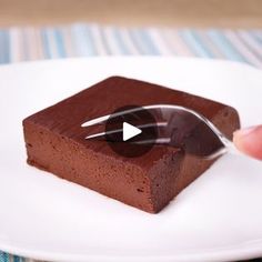 a piece of chocolate cake on a white plate with a spoon in it and someone's thumb touching the top