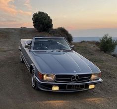 a car parked on the side of a dirt road near a tree and water at sunset