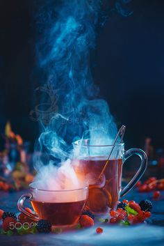 two mugs filled with hot tea and steam rising out of them, surrounded by berries