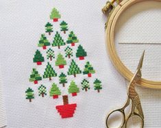 a cross stitch christmas tree with red and green trees on it, next to a pair of scissors