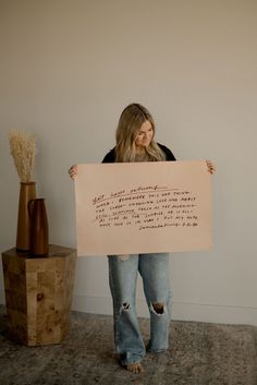 a woman holding up a sign with writing on it in front of a wooden vase