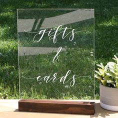 a glass sign that says gifts and cards on it next to a potted plant